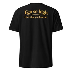 May include: Black t-shirt featuring gold text on the back. The text says "Ego so high" above the phrase "I love that you hate me". The shirt is a short-sleeved, casual style.