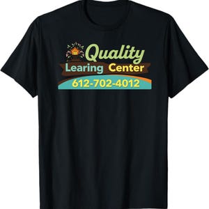 May include: Black t-shirt with a colorful graphic. The graphic includes the words "Quality Learning Center" in green and yellow, a small house illustration, and a phone number. The shirt is made of a soft material.