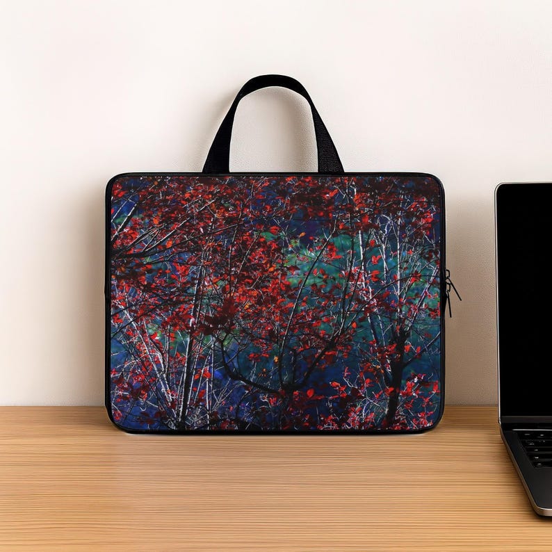 Puede incluir: Funda negra para port&aacute;til con una imagen de un bosque con hojas rojas sobre un fondo azul y verde. Tiene un asa negra y cierre de cremallera. Un port&aacute;til est&aacute; sobre una superficie de madera. La funda protege el port&aacute;til.