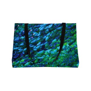May include: A tote bag featuring a vibrant, abstract design of blue and green leaves. The bag has black handles and a rectangular shape. The leaves have a gradient effect, transitioning from dark blue to light green.