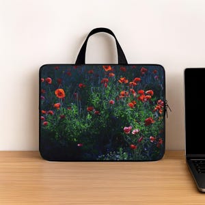 May include: A rectangular laptop sleeve featuring a photographic print of vibrant red poppy flowers set against a dark, moody green foliage background. The sleeve has black trim, a black zipper closure, and a single black handle at the top center.