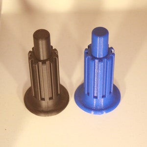 Op de afbeelding: Twee plastic knoppen, een zwarte en een blauwe, met een geribbeld ontwerp. De knoppen worden gebruikt voor meubels.