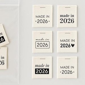 Może przedstawiać: Zestaw kwadratowych, kremowych etykiet z tkaniny z napisem "MADE IN 2026" w różnych czarnych krojach pisma, w tym z sercami, kropkami lub ramkami. Cztery etykiety znajdują się w przezroczystej plastikowej torebce, a sześć jest ułożonych obok.