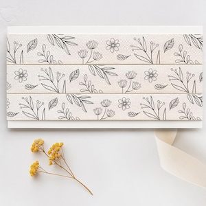 Puede incluir: Una cinta blanca con un patr&oacute;n floral negro. La cinta est&aacute; hecha de un tejido suave y tejido y presenta un dise&ntilde;o delicado de hojas y flores.