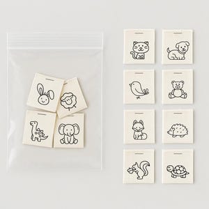 Puede incluir: Un conjunto de pequeñas etiquetas de tela blanquecina con dibujos lineales negros de varios animales, como un gato, un perro, un pájaro, un oso, un zorro, un erizo, una ardilla y una tortuga. Algunas etiquetas están en una bolsa de plástico transparente.