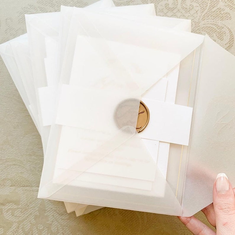 May include: A stack of white envelopes with a gold wax seal. The envelopes are layered on top of each other and are ready to be mailed.