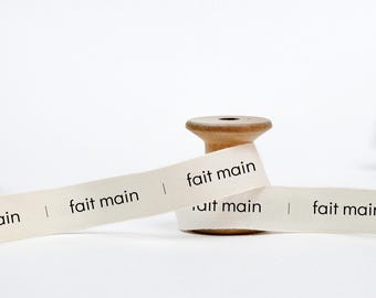 May include: A spool of white cotton ribbon with the text "fait main" printed on it. The ribbon is wrapped around a wooden spool.