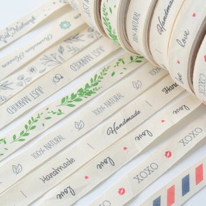 Puede incluir: Surtido de rollos de cinta de algod&oacute;n natural con varios dise&ntilde;os y textos, incluyendo "Just Married", "Handmade", "Love" y "XOXO".