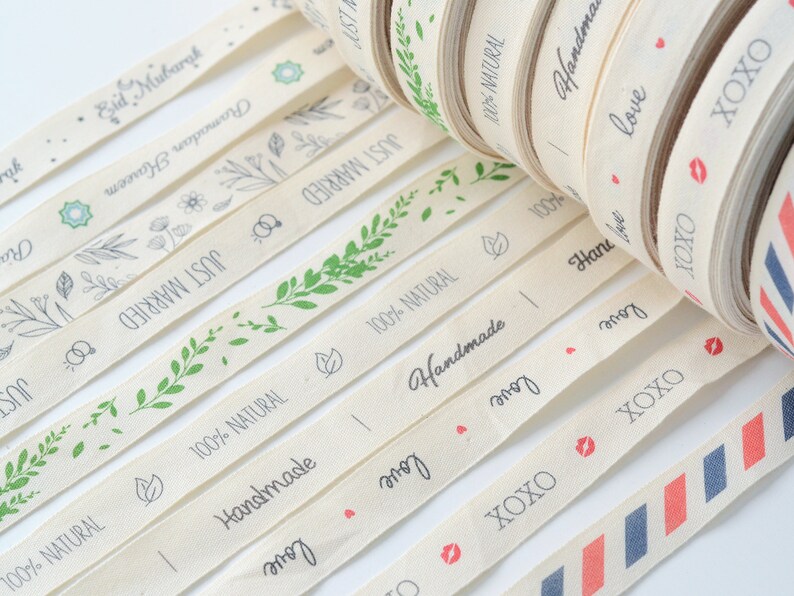 Puede incluir: Surtido de rollos de cinta de algod&oacute;n natural con varios dise&ntilde;os y textos, incluyendo "Just Married", "Handmade", "Love" y "XOXO".