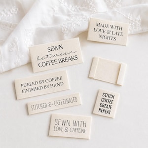 May include: A collection of rectangular cream-colored fabric clothing labels with black text. The labels feature phrases including MADE WITH LOVE & LATE NIGHTS, SEWN between COFFEE BREAKS, FUELED BY COFFEE FINISHED BY HAND, STITCHED & CAFFEINATED, SEWN WITH LOVE & CAFFEINE, and STITCH COFFEE CREATE REPEAT.