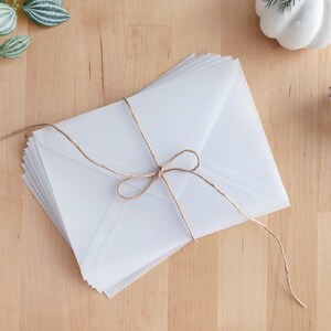May include: A stack of white envelopes tied together with twine. The envelopes are on a light wood surface.