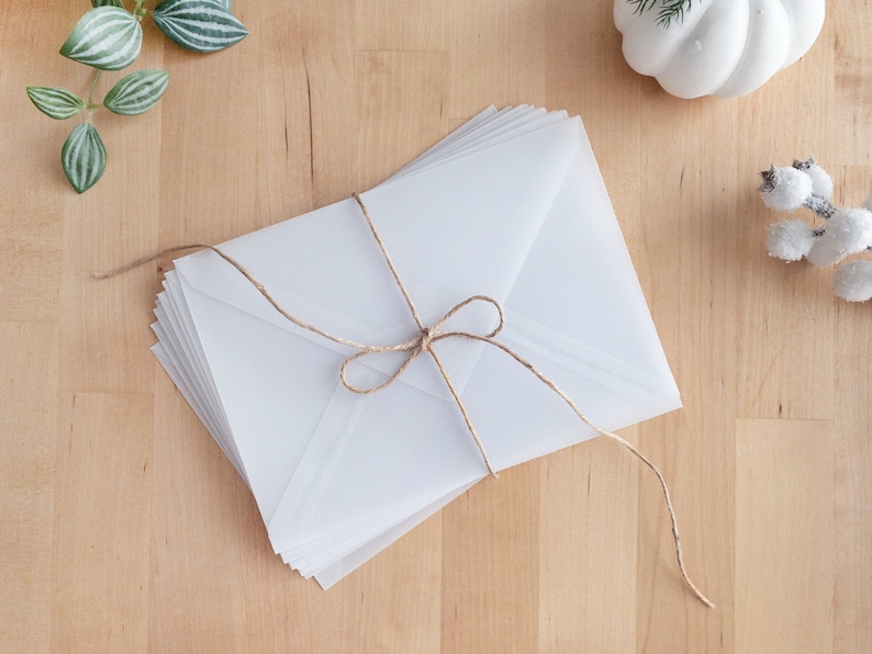 May include: A stack of white envelopes tied together with twine. The envelopes are on a light wood surface.