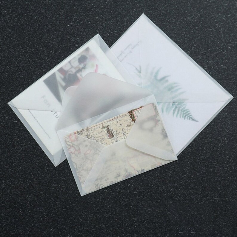 May include: Three translucent white envelopes with a frosted finish. The envelopes are layered on top of each other. The top envelope has a fern design printed on it. The middle envelope has a vintage map design printed on it. The bottom envelope has a floral design printed on it.