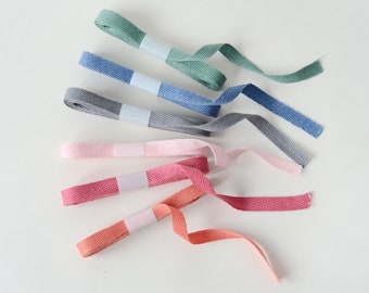 May include: Assortment of six cotton twill ribbon in various colors, including pink, red, gray, blue, and green. The ribbon is flat and has a herringbone pattern.