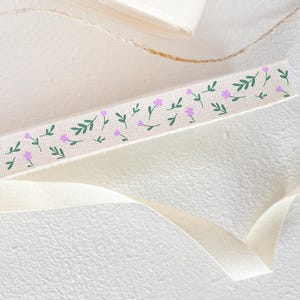 Puede incluir: Una cinta blanca con un patrón repetido de pequeñas flores rosas y hojas verdes.