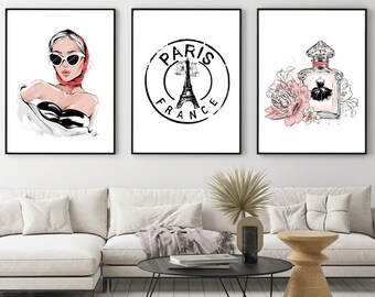 May include: Three black framed prints with white backgrounds. The left print features a black and white illustration of a woman wearing sunglasses and a red headscarf. The middle print features a black and white illustration of the Eiffel Tower with the text "Paris France" in a circle around it. The right print features a black and white illustration of a perfume bottle with pink flowers.