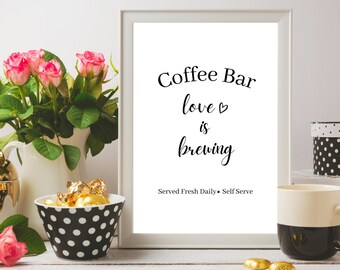 May include: A white framed sign with black text that reads "Coffee Bar love is brewing" and "Served Fresh Daily - Self Serve". The sign is on a white shelf with pink roses, a gold teapot, a black and white polka dot bowl with gold chocolate candies, and a black and white mug.