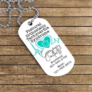 Puede incluir: Collar con placa de alerta m&eacute;dica blanca con un coraz&oacute;n azul y un s&iacute;mbolo m&eacute;dico. La placa dice "S&iacute;ndrome de taquicardia ortost&aacute;tica postural" y "Contactos de emergencia: Esposo: 813-444-6792 Mam&aacute;: 727-999-8972".