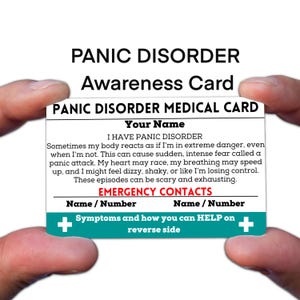 May include: A white and teal Panic Disorder Medical Card held between two hands. The card includes the text "PANIC DISORDER MEDICAL CARD", "Your Name", and a description of panic disorder symptoms. It also has space for emergency contacts.