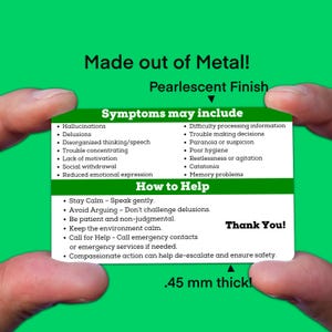 May include: A white card with blue and green text lists symptoms and how to help someone experiencing a mental health crisis. The card is made of metal and is 0.45 mm thick. The text on the card reads "Made out of Metal! Pearlescent Finish" and "Thank You!"