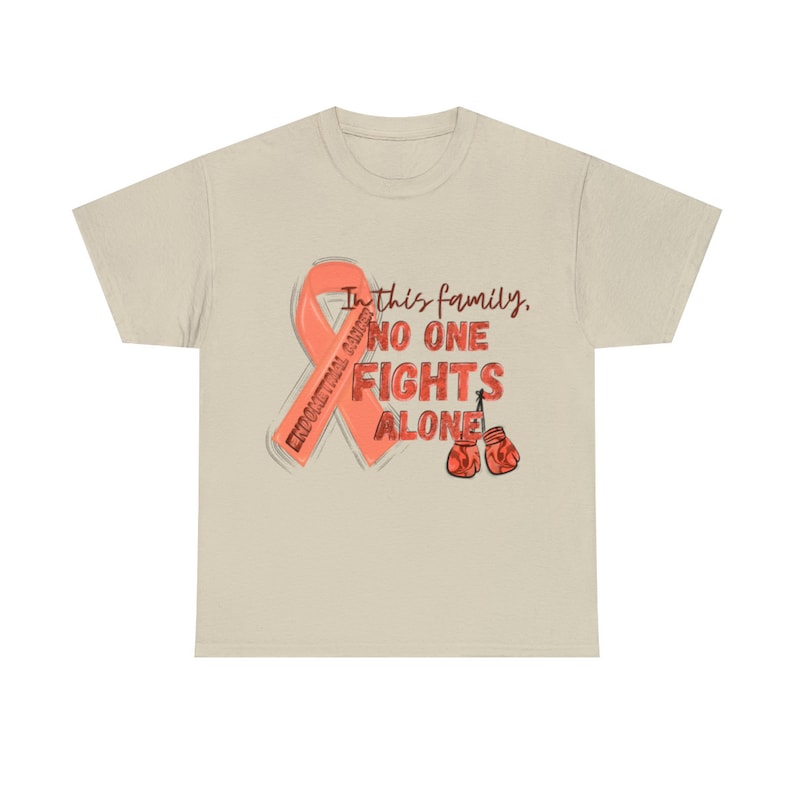 May include: A beige t-shirt featuring a pink ribbon and the text "In this family, no one fights alone". The ribbon has the words "Endometrial Cancer" written on it. Two red boxing gloves are depicted below the text.