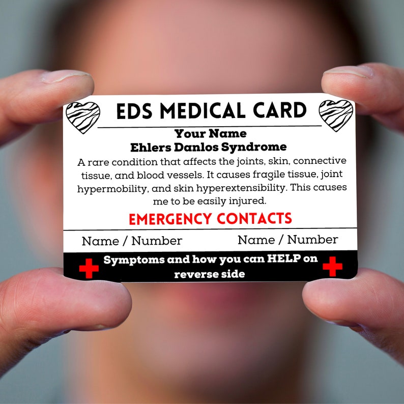 May include: A white card with black text that reads "EDS MEDICAL CARD". The card has a red heart with a black and white zebra pattern on each side. The text on the card reads "Your Name Ehlers Danlos Syndrome" and "A rare condition that affects the joints, skin, connective tissue, and blood vessels. It causes fragile tissue, joint hypermobility, and skin hyperextensibility. This causes me to be easily injured." The card also has the text "EMERGENCY CONTACTS" and "Name / Number" twice. The card has a red plus sign on each side with the text "Symptoms and how you can HELP on reverse side".