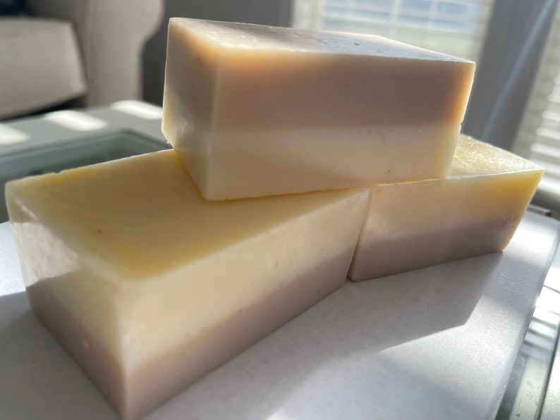 May include: Three bars of layered soap, each with a white top layer and a light brown bottom layer. The bars are stacked on top of each other.