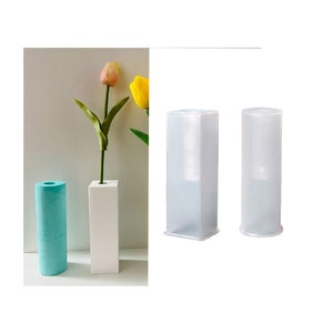Peut inclure: Deux moules à vase en plastique transparent, un carré et un rond, pour la fabrication de vases en béton ou en résine. Les moules sont présentés à côté d'un vase blanc avec une seule tulipe rose et jaune.