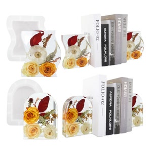 May include: Two clear resin bookends shaped like arches, each containing pressed flowers. The flowers are yellow, white, and red. The bookends are holding up two books with the titles "FOLIO-02", "AURORA FOLKLORE", "CREATE WONDERFUL HOMELIFE", "HOMES", and "SPECIAL ISSUE".