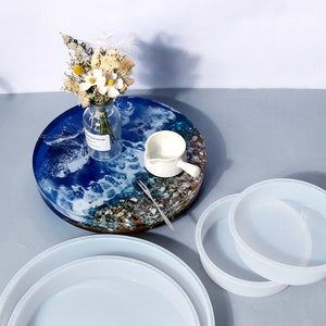 May include: Three round silicone molds for resin casting, in different sizes. The molds are white and are sitting on a table with a blue and white resin tray with a flower arrangement on top.