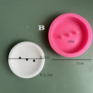 May include: Two round silicone molds for making concrete planters. The larger mold is pink and measures 11 inches in diameter. The smaller mold is white and measures 9.9 inches in diameter. Both molds have three holes in the bottom for drainage.