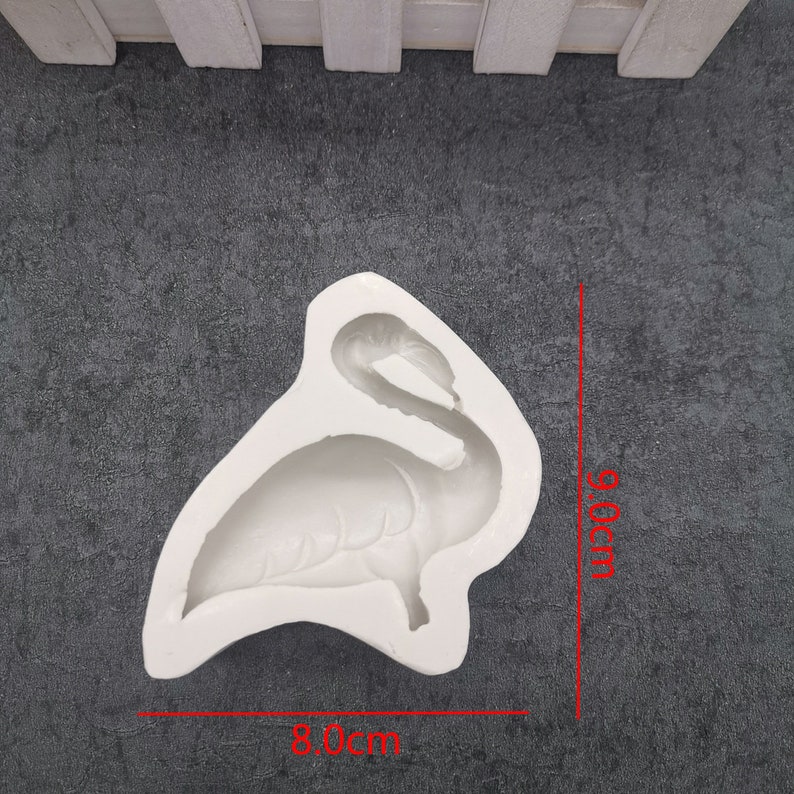 May include: A white silicone mold in the shape of a flamingo, measuring approximately 3.1 inches wide and 3.8 inches tall. The mold is designed for creating decorative items, likely for baking or crafting projects.