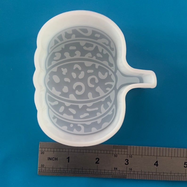 May include: A clear, flexible silicone mold in the shape of a pumpkin with a handle. The pumpkin design features a leopard print pattern. A metal ruler is placed next to the mold, showing inch measurements.