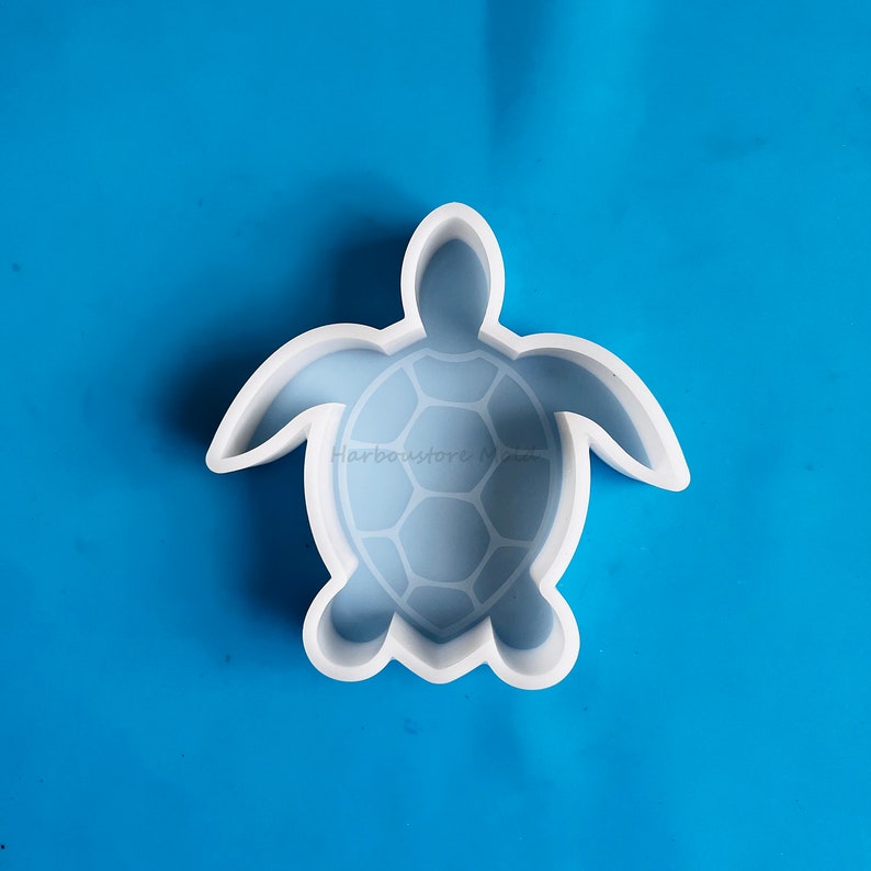 Puede incluir: Un molde de silicona blanco con forma de tortuga, con un patr&oacute;n de caparaz&oacute;n detallado. El molde est&aacute; sobre un fondo azul brillante. El texto "Harbourstore Molds" es visible en el molde.