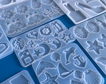 May include: A set of clear silicone molds for making resin jewelry. The molds feature various shapes, including stars, moons, seashells, and a dolphin. The molds are perfect for creating unique and personalized jewelry pieces.
