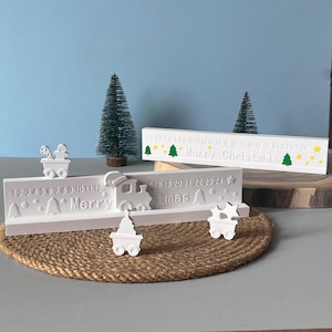 Könnte beinhalten: Weißer Weihnachtskalender mit einem Zugdesign. Der Kalender zeigt die Zahlen 1-24, den Text "Merry Christmas" und kleine dekorative Elemente. Der Kalender wird auf einer gewebten Matte präsentiert.