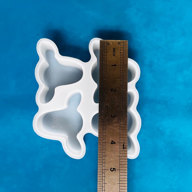 Op de afbeelding: Witte siliconen mal met vier hartvormige holtes. De mal is ongeveer 5 inch lang en wordt naast een liniaal getoond.