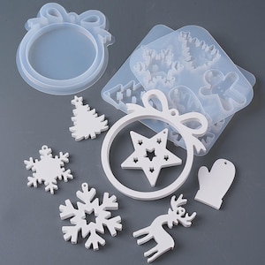 Pode incluir: Uma coleção de moldes de resina e enfeites acabados com tema natalino branco. Os moldes incluem flocos de neve, um boneco de gengibre e uma árvore de Natal. Os enfeites acabados incluem um enfeite em forma de estrela, uma rena e uma luva.