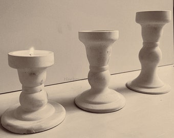 May include: Three white candle holders with a simple design. The candle holders are made of a textured material and have a round base. The candle holders are arranged in a row on a white surface.