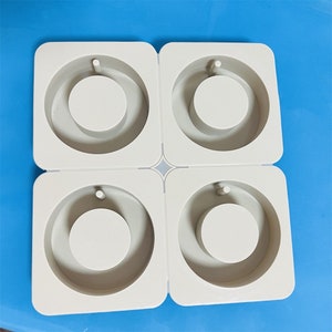 Puede incluir: Cuatro moldes de silicona blancos para hacer joyas de resina. Cada molde tiene una forma circular con un círculo más pequeño en el centro para un colgante o un amuleto.