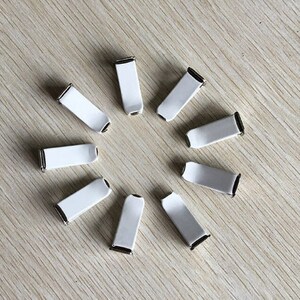 Op de afbeelding: Tien witte plastic clips met een zilveren metalen bevestiging. De clips zijn in een cirkel op een lichtbruin houten oppervlak gerangschikt.
