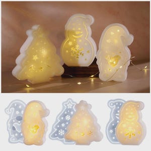 May include: Three illuminated Christmas decorations: a tree, a snowman, and a gnome. Each is white and emits a warm glow. The tree has star-shaped cutouts, the snowman has a snowflake, and the gnome has a heart. A string of lights is in the background.