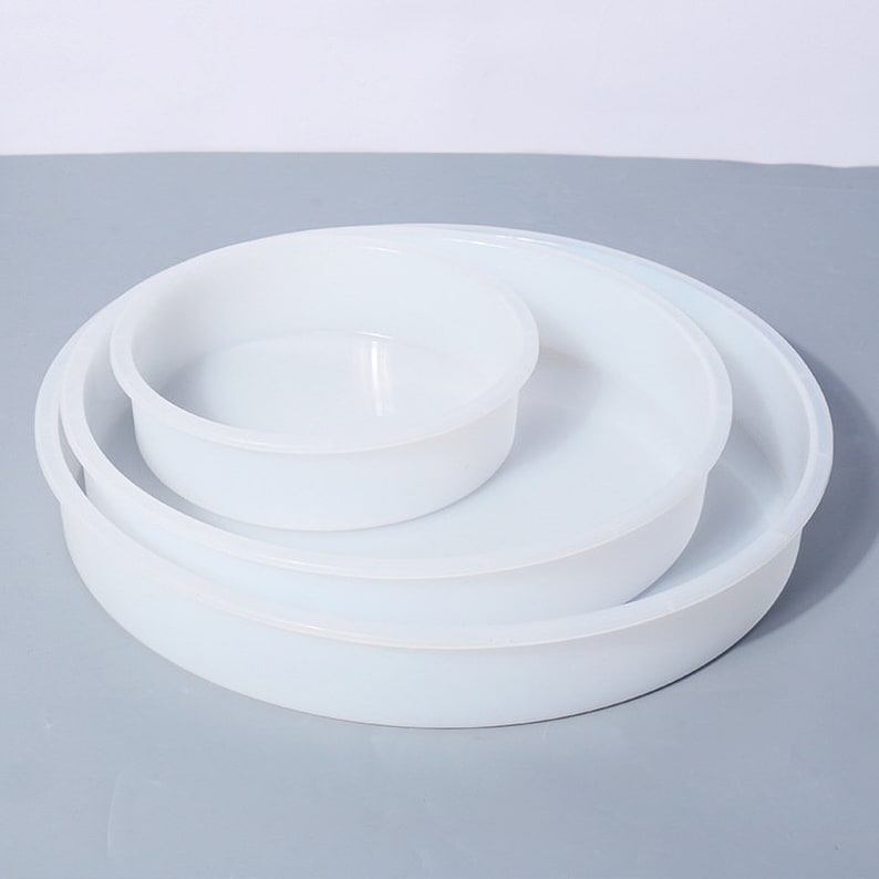 May include: Three white plastic round cake pans of different sizes stacked on top of each other.