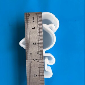May include: A white, bird-shaped silicone mold, approximately 4 inches in height, is shown against a blue background. A metal ruler is placed next to the mold for measurement. The mold is likely for crafting or baking.