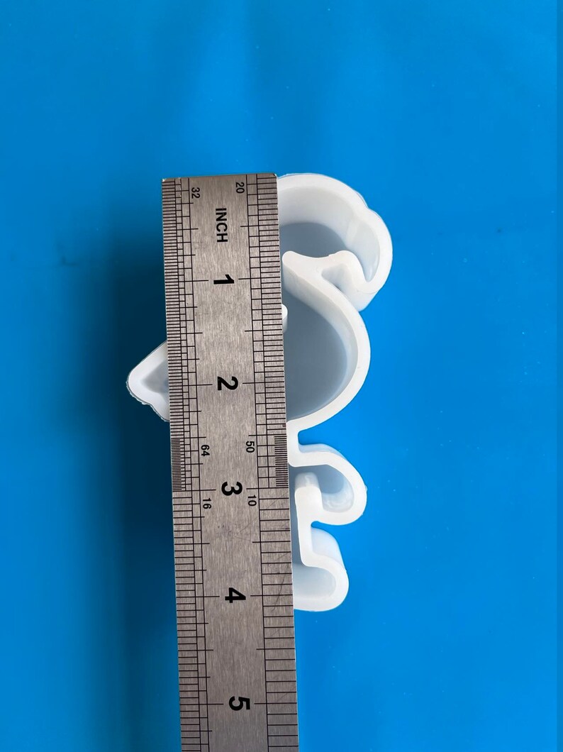 May include: A white, bird-shaped silicone mold, approximately 4 inches in height, is shown against a blue background. A metal ruler is placed next to the mold for measurement. The mold is likely for crafting or baking.