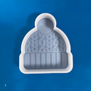May include: White silicone mold shaped like a knitted winter hat. The mold has a textured design to resemble a knitted pattern.