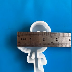 May include: A white silicone mold in the shape of a stick figure with a bow tie. The mold is approximately 3 inches tall. The mold is on a blue surface.