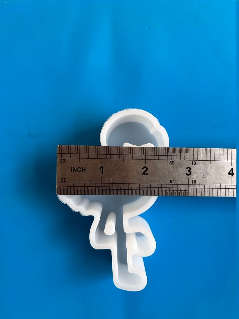 May include: A white silicone mold in the shape of a stick figure with a bow tie. The mold is approximately 3 inches tall. The mold is on a blue surface.