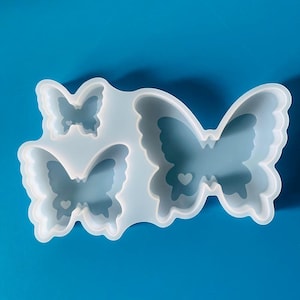May include: A clear, flexible silicone mold with three butterfly-shaped cavities. The cavities vary in size and feature heart-shaped details. The mold is set against a bright blue background.