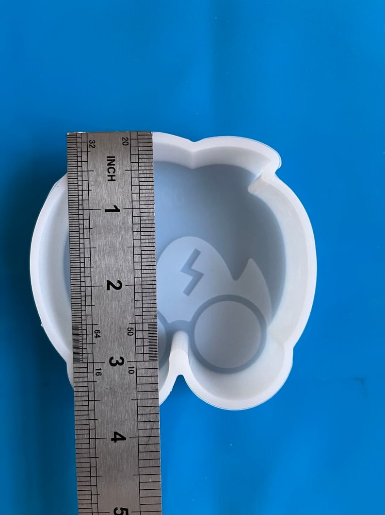 May include: A white silicone mold in the shape of a cartoon owl with a lightning bolt and round glasses. The mold is approximately 3 inches wide, as measured by a ruler.